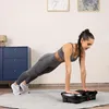 A woman is doing a plank exercise on a vibration plate in a room. Produktbild-Vorschau