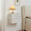 A floating nightstand with two drawers, featuring a marble-like finish, is mounted on a white wall next to a bed. A small table lamp with a pleated shade and a cup of tea are placed on top of the nightstand. Anteprima dell’immagine prodotto