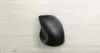 A black computer mouse is placed on a light-colored wooden surface. Voir les images du produit
