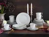 A formal table setting with white porcelain dinnerware, gold cutlery, and candles. Produktbild-Vorschau