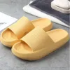 Paar gelbe gepolsterte Schlapfen auf grauer Fläche neben gefalteten Handtüchern und Seifenschale Anteprima dell’immagine prodotto