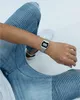 A person wearing a silver digital watch on their wrist, paired with blue jeans. Produktbild-Vorschau