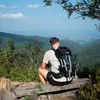 A person sitting on a bench overlooking a valley, wearing a backpack. Anteprima dell’immagine prodotto