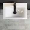 A top-down view of a white ceramic sink with a black faucet, placed on a tiled floor. Produktbild-Vorschau