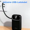 A black power bank is plugged into a white wall socket with a USB cable. The power bank displays '100%' on its screen. Produktbild-Vorschau