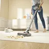 A person is using a cordless vacuum cleaner to clean up a mess on a rug, while a white cat watches. Produktbild-Vorschau
