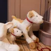 A close-up of two toy dogs on a wooden floor, with stacked boxes in the background. Anteprima dell’immagine prodotto