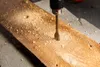 A drill bit is drilling a hole in a wooden plank, creating sawdust. Podgląd zdjęcia produktu