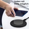 A hand is placing a smartphone onto a black wireless charging pad on a white table. Produktbild-Vorschau