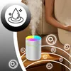 A humidifier with a colorful LED light is shown on a wooden surface next to a person. Oxygen symbols are scattered around the image. Produktbild-Vorschau