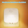 A white plug-in night light with a motion sensor is plugged into a wall socket, emitting a warm light. Produktbild-Vorschau