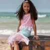 Mädchen trägt Meerjungfrauenkostüm und sitzt lächelnd auf einer alten Schatztruhe am Strand mit Meer im Hintergrund. Produktbild-Vorschau