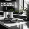 A modern kitchen counter with a silver rice cooker as the main focus, surrounded by plants and kitchenware. Náhled obrázku produktu
