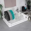 A white dish rack filled with plates, glasses, and cutlery next to a sink. Produktbild-Vorschau