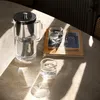 A glass pitcher with a filter and two glasses on a marble table, with sunlight casting shadows. Náhľad obrázku produktu