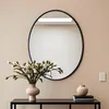 A round mirror hangs on a wall above a console table with a vase of flowers and decorative vases. Podgląd zdjęcia produktu