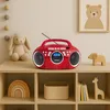 A red boombox sits on a wooden shelf next to a stuffed bunny and a wooden elephant. The shelf is part of a larger shelving unit with other decorative items. Produktbild-Vorschau