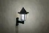 A black outdoor wall lamp is mounted on a textured gray wall. Produktbild-Vorschau