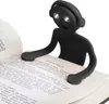 A black book light shaped like a person with headphones is clipped onto an open book. Voir les images du produit