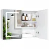 A white bathroom cabinet with its doors open, displaying shelves stocked with toiletries and accessories. The left side of the cabinet features a mirrored door with a reflection of a plant and a bathtub, illuminated by a modern LED light strip. Produktbild-Vorschau