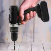 A hand holding a black cordless drill, with the drill bit touching a wooden surface. Produktbild-Vorschau