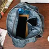 The inside of a blue handbag is shown, with a water bottle, tablet, and phone inside. Produktbild-Vorschau