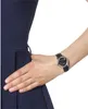 A close-up of a woman's wrist wearing a black leather watch with a silver case and black dial, next to a navy blue dress. Produktbild-Vorschau