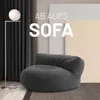 A dark gray beanbag sofa is placed on a rug in a room with dark curtains and light-colored panels in the background. A floor lamp is to the left. Náhľad obrázku produktu