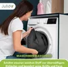 A woman is putting a dark grey item into a washing machine. There are two bottles of laundry detergent on top of the washing machine. Produktbild-Vorschau