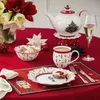 A festive Christmas table setting with a teapot, mug, bowl, plate, and champagne glass on a red tablecloth. Náhled obrázku produktu