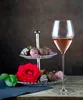 A glass of rosé wine sits next to a tiered stand of chocolate-covered strawberries and a red rose. Podgląd zdjęcia produktu