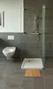 A modern bathroom with a toilet, shower, and a bamboo bath mat. Produktbild-Vorschau