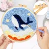 A person's hands are shown working on a punch needle embroidery kit featuring a whale design. A close-up inset shows the embroidery hoop's tensioning mechanism. Produktbild-Vorschau