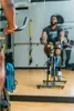 A person is exercising on a stationary bike in a gym, with a water bottle attached to the bike. Produktbild-Vorschau