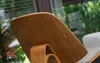 Close-up of the back of a wooden designer chair with a beige cushion visible. Voir les images du produit