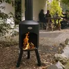 People gathered around a table on a patio with a fire pit in the foreground. Produktbild-Vorschau