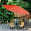 An outdoor patio scene with tables and chairs under a large orange umbrella. Produktbild-Vorschau