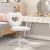 A white heart-shaped fluffy chair in a bedroom setting, next to a bed and a vanity table. Podgląd zdjęcia produktu