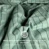Close-up of green fabric with black stripes, folded and creased, with a circular overlay containing a cloud and feather icon and text. Produktbild-Vorschau