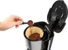 A person's hand is adding ground coffee to a coffee filter in a coffee maker. Anteprima dell’immagine prodotto