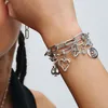 A close-up shot of a person's arm wearing a silver charm bracelet with various charms including a heart, a hamsa hand, a spade, and a spiral. Anteprima dell’immagine prodotto