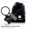 A black motorcycle keychain with a velvet bag and a tag with German text. Produktbild-Vorschau