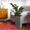 A tall, gray, textured planter with a green plant sits on a wooden floor next to a beige armchair and a wooden cabinet. A small side table with a yellow top is visible on the right. Náhled obrázku produktu