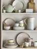 A collection of ceramic tableware, including teapots, cups, plates, and bowls, arranged on shelves. Produktbild-Vorschau