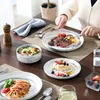 A table setting with various dishes, including steak, salad, pasta, and dessert, with a person's hands visible preparing to eat. Produktbild-Vorschau