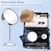 A makeup mirror is shown with its base removed, indicating its portability for travel, and packed inside a suitcase with travel essentials. Produktbild-Vorschau