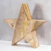 A wooden star decoration is placed on a white surface against a gray concrete wall. Produktbild-Vorschau