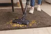 A person is vacuuming cereal off a brown carpet with a cordless vacuum cleaner. Voir les images du produit