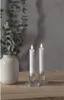 Two LED candles in glass holders are placed on a wooden table, with a vase of eucalyptus leaves in the background. Produktbild-Vorschau