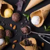 A top-down view of ice cream cones, scoops of ice cream, chocolate pieces, almonds, and chocolate chips on a black surface. Náhľad obrázku produktu